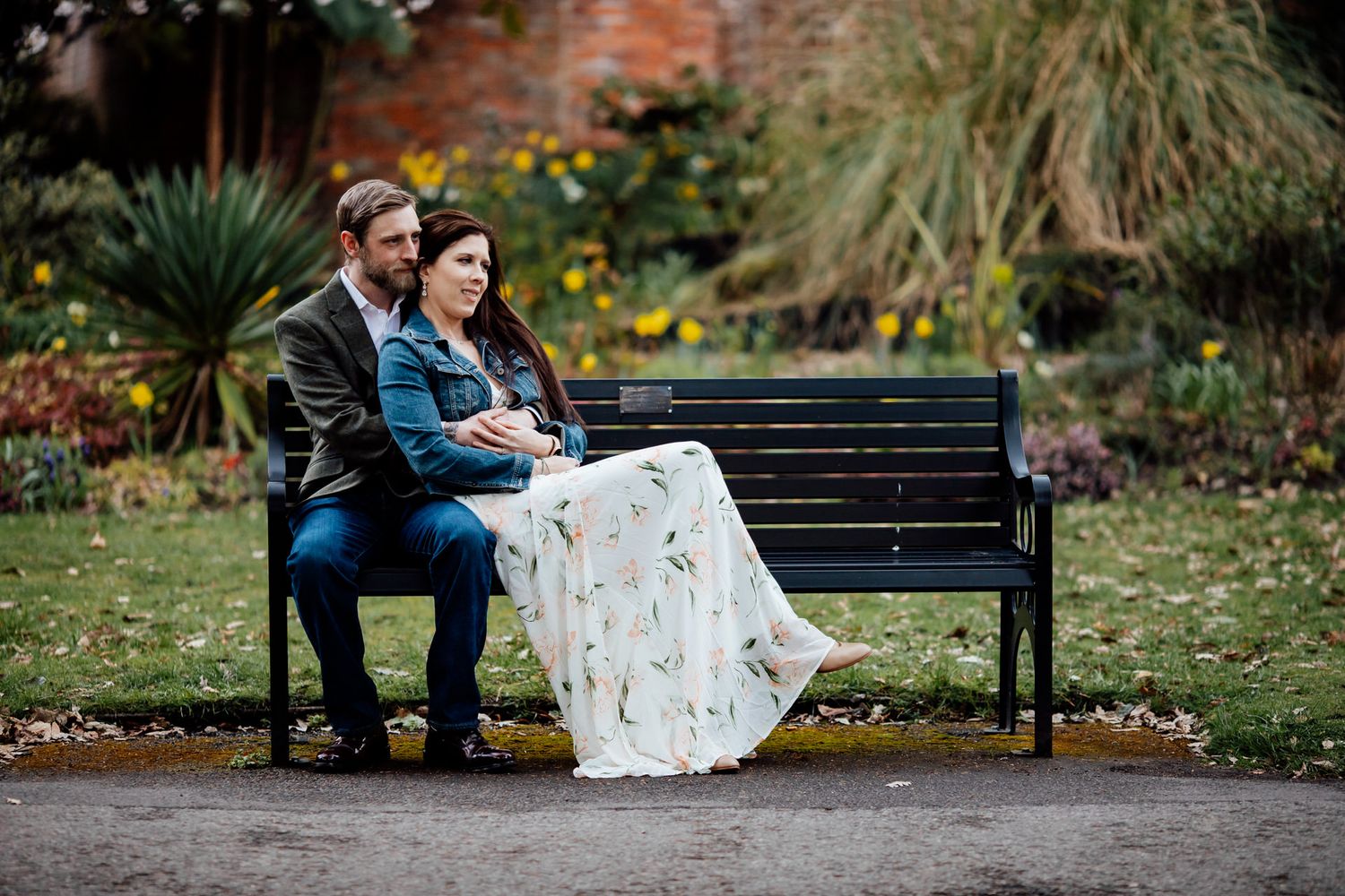 A couple sits together on a park bench surrounded by autumn foliage.