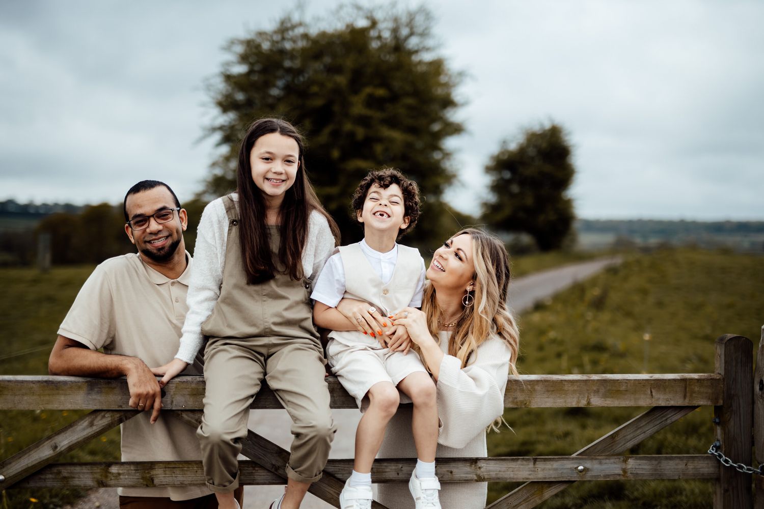 A family in neutral tones poses together outdoors on a rustic wooden bench.