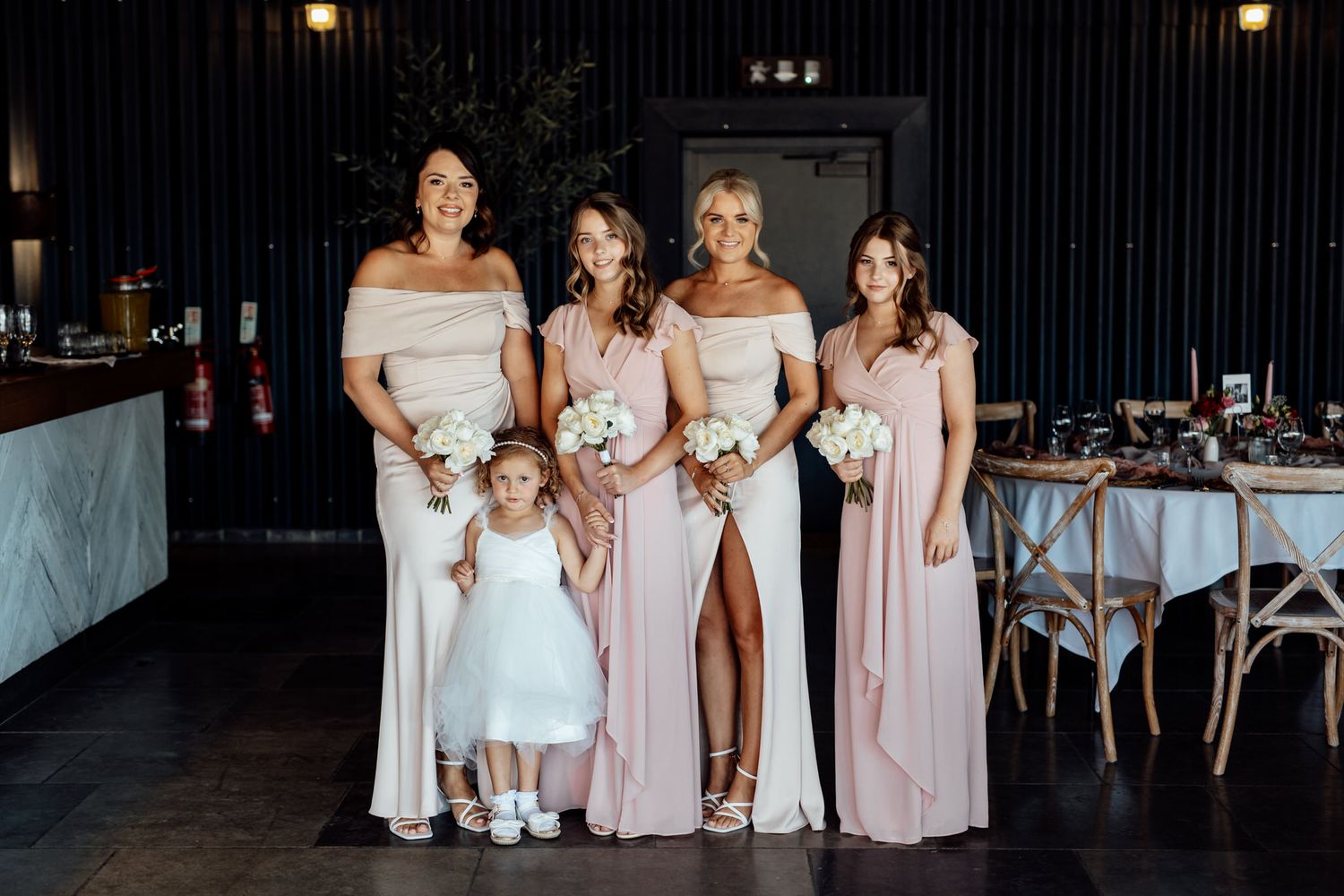 Bridesmaids in light pink dresses pose together at evening wedding celebration.