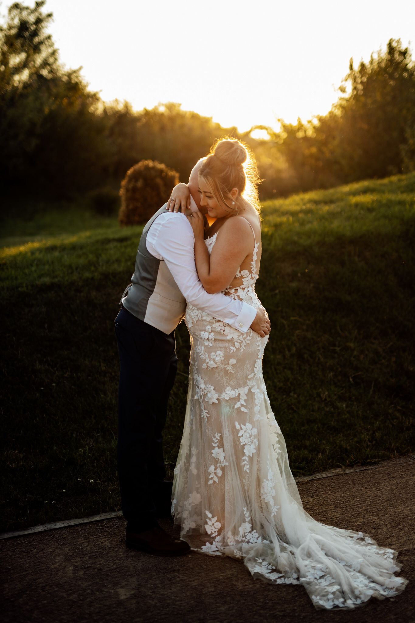 Romantic sunset wedding portrait with flowing lace dress against golden light.