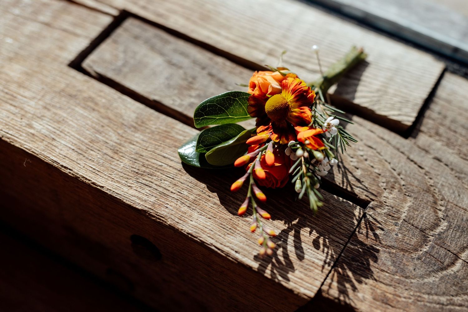 Autumn-colored floral arrangement with orange blooms on weathered wooden surface.
