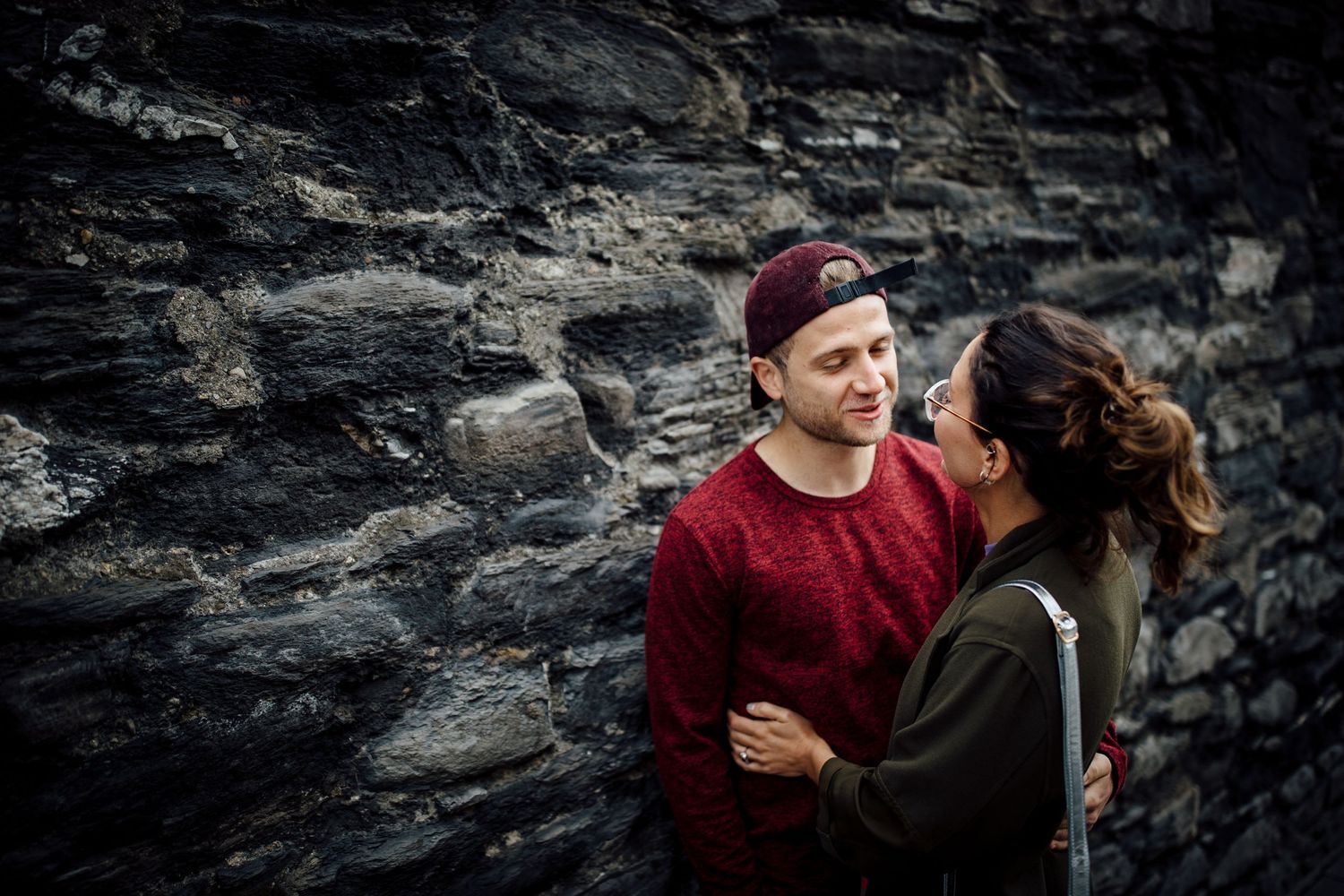 Romantic portraits against dramatic rocky wall backdrop in moody lighting.