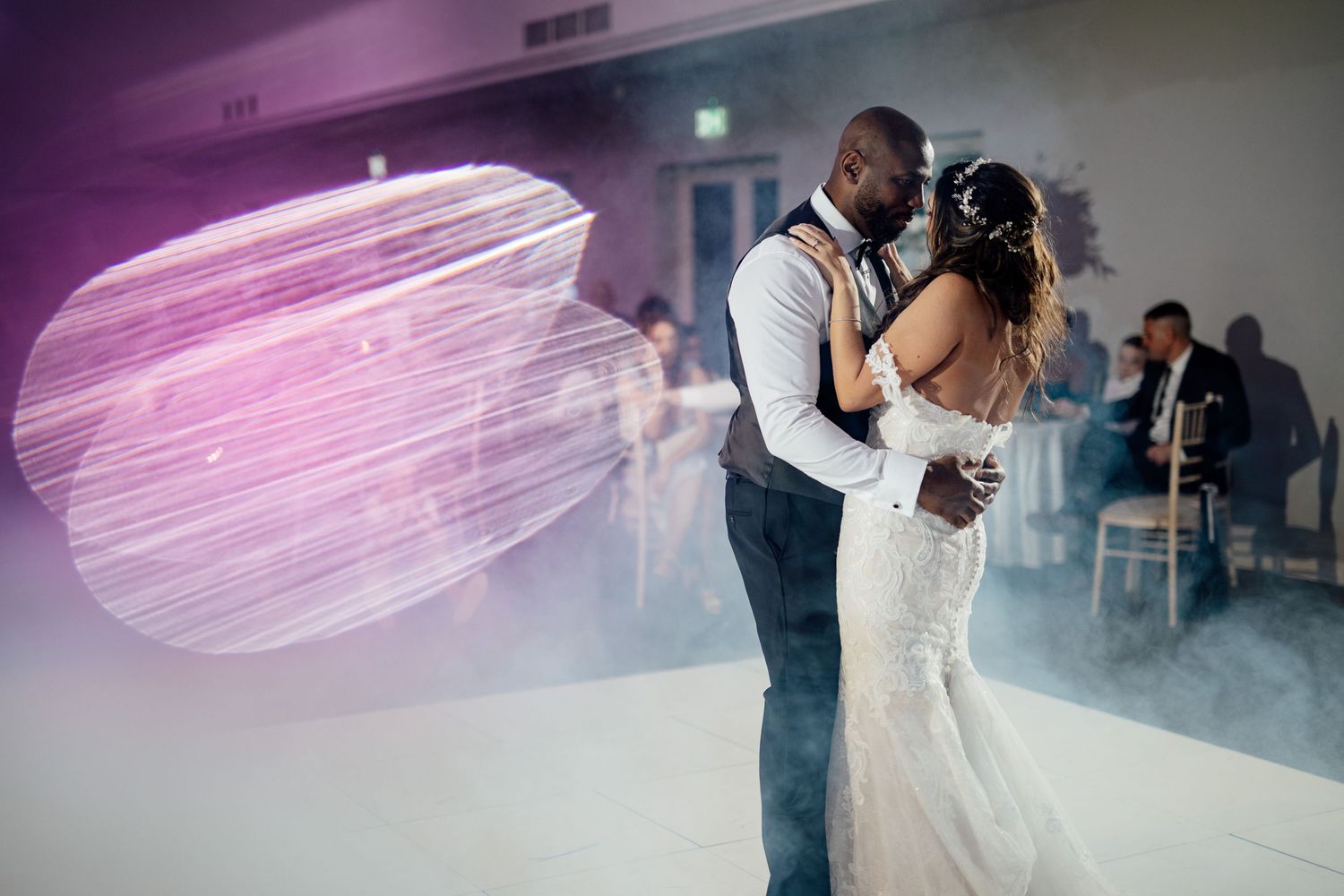 Wedding couple dancing under purple lighting at indoor reception.
