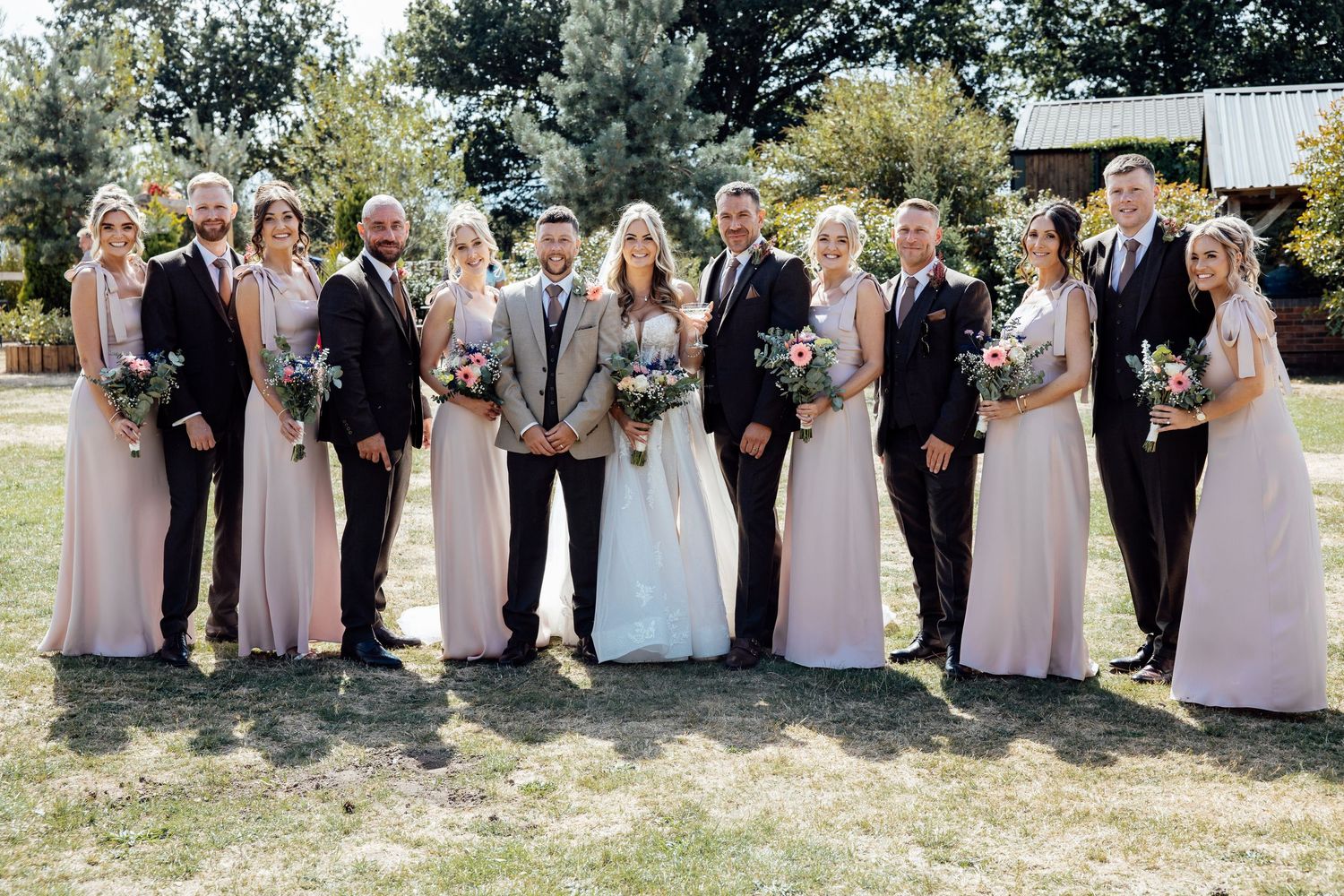 Wedding party posing outdoors in blush bridesmaid dresses and navy suits with bride and groom center.