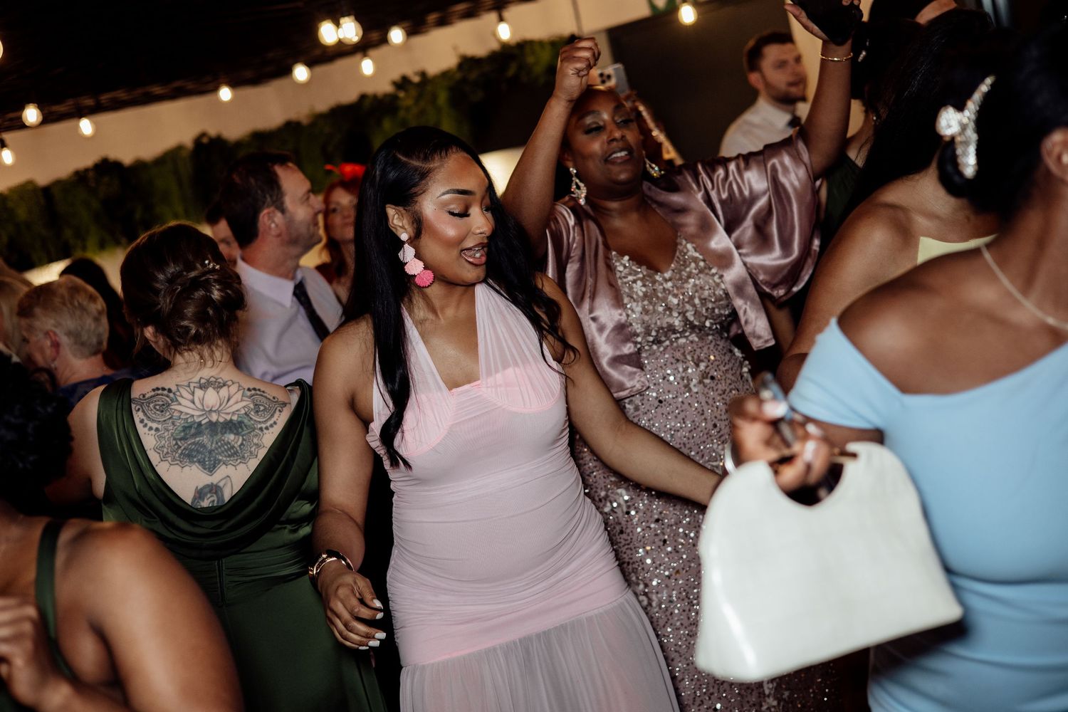 Wedding guests in colorful dresses dance joyfully together at an outdoor evening wedding reception.