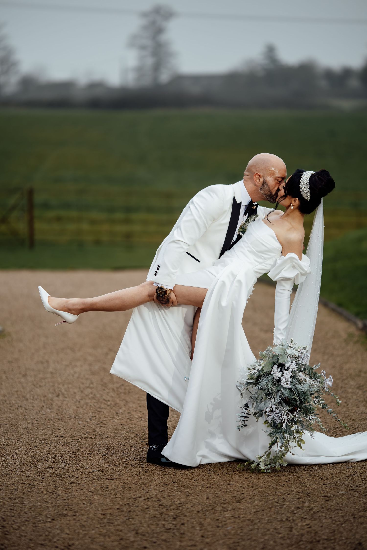 Elegant wedding couple posing for dramatic dip photos on a gravel path with greenery in background.
