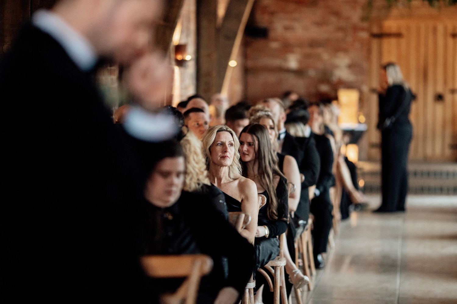 Wedding ceremony guests seated in rows at an indoor rustic brick venue.