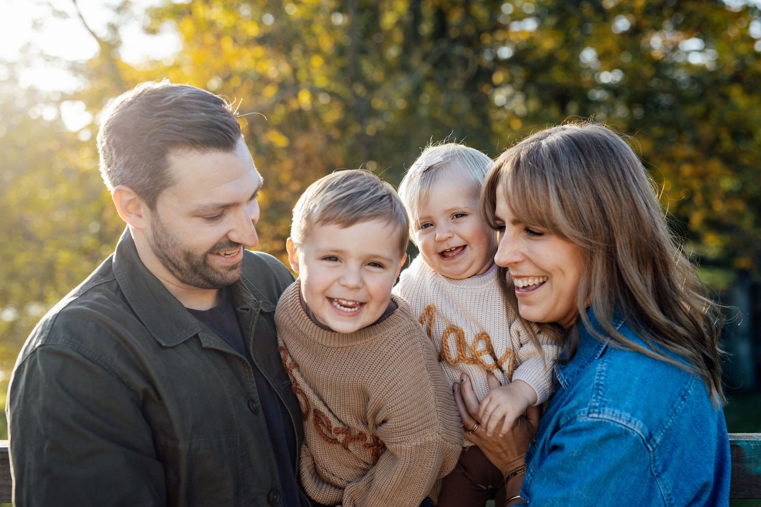A family shares joyful moments together during an autumn outdoor photo session with golden foliage in the background.