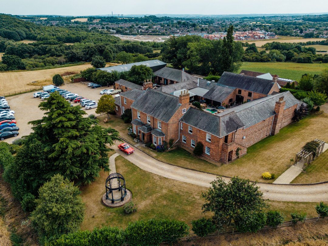 Aerial view of a red brick wedding venue with parking area and surrounding countryside.