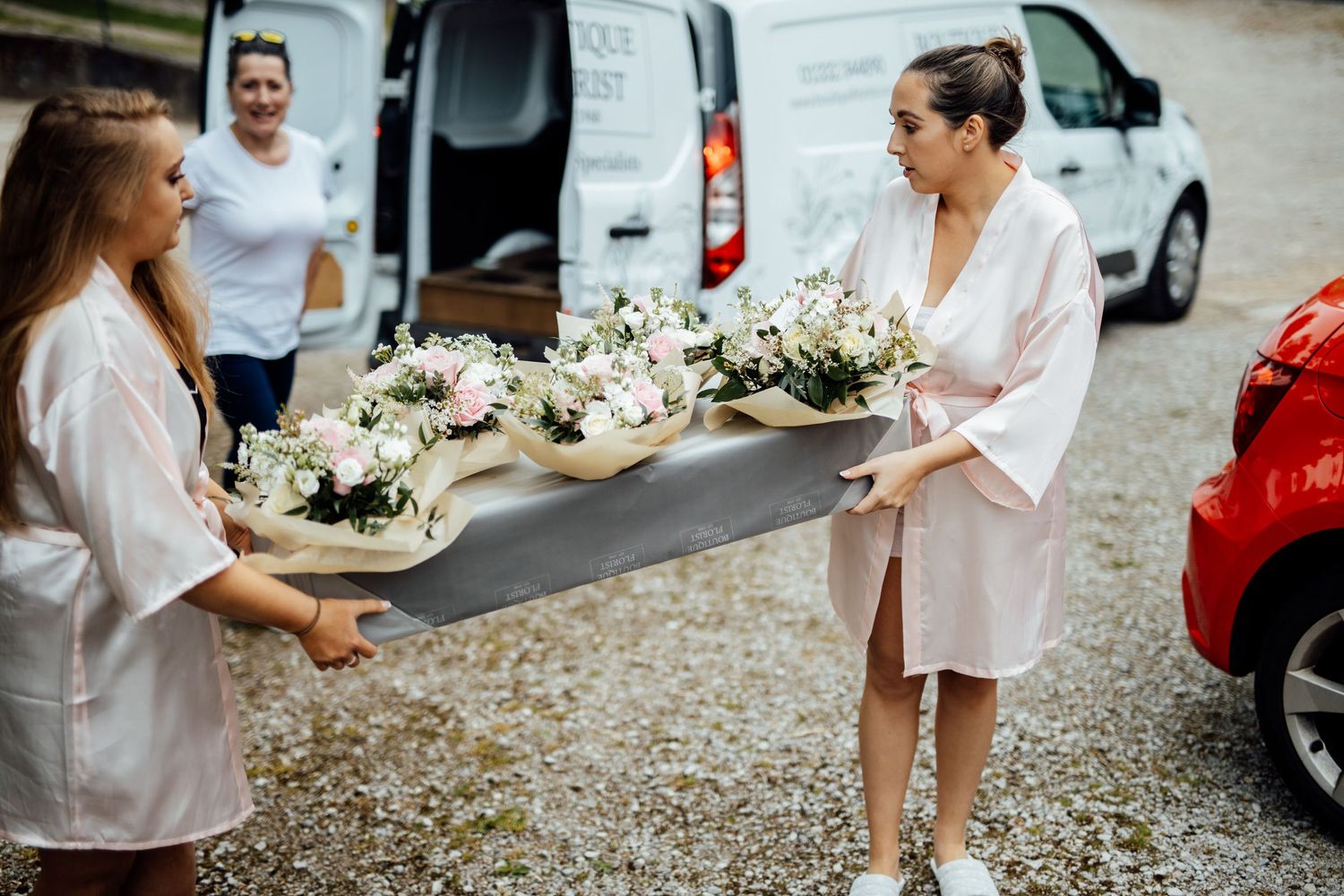 Wedding party members walk casually down a gravel path carrying bouquets.
