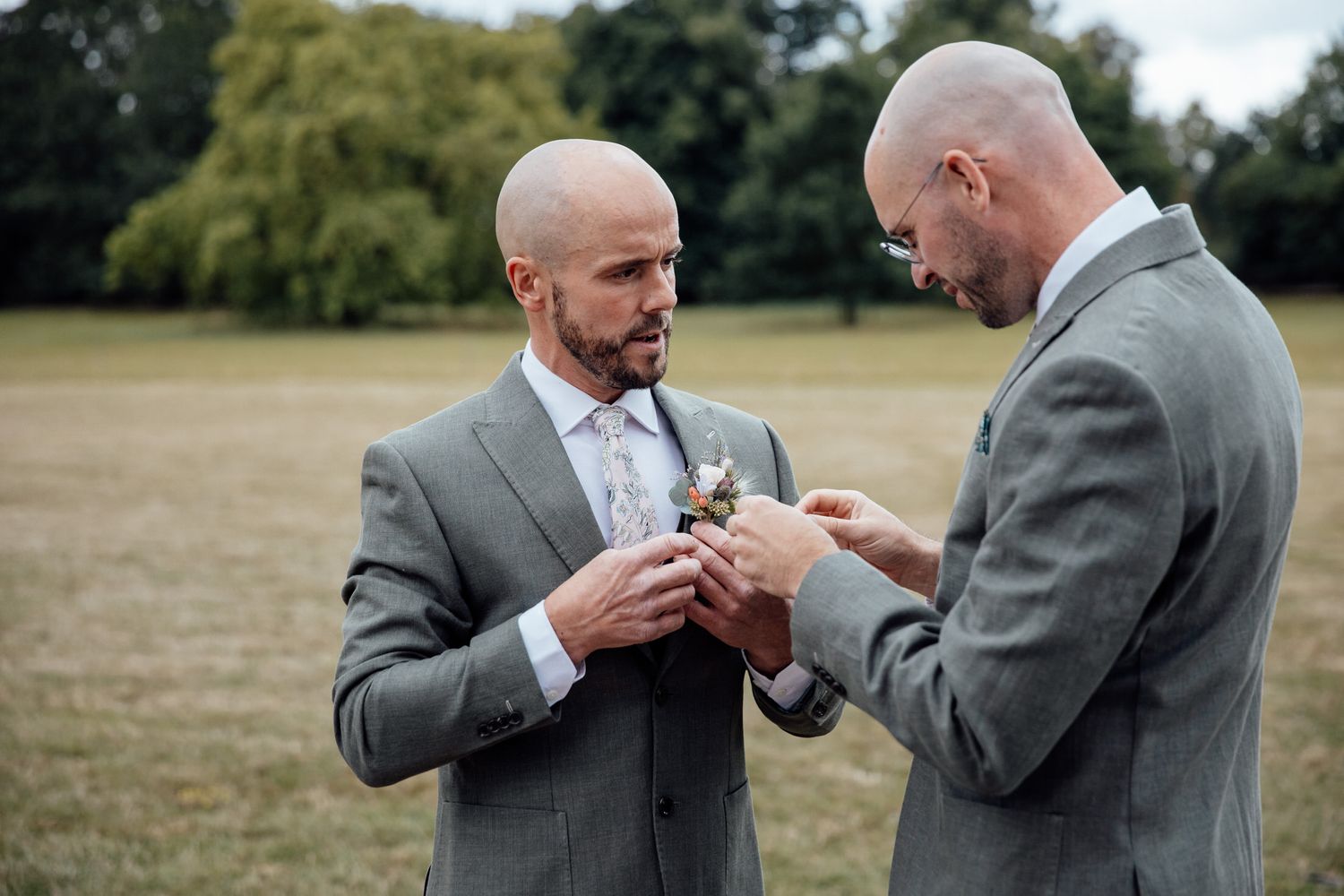Groomsmen adjusting ties and helping with formal attire outdoors.