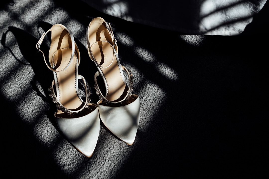 Elegant cream-colored wedding shoes with decorative details in dramatic lighting.
