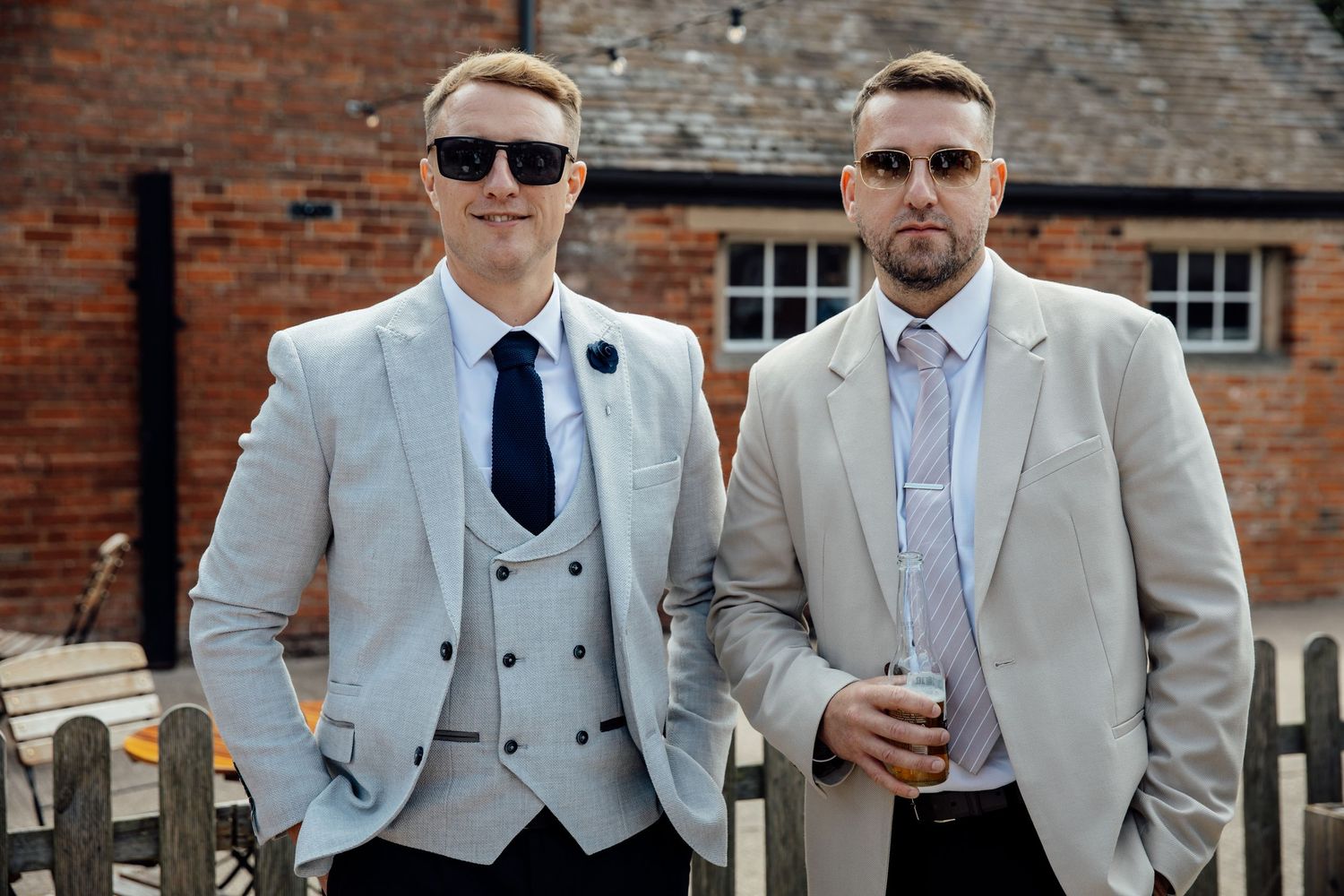 Groomsmen in light grey suits pose together against brick wall backdrop.