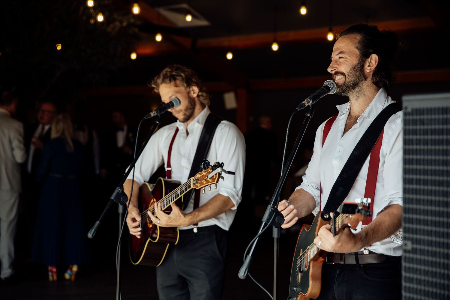 Live band performs with acoustic guitars at evening wedding reception.