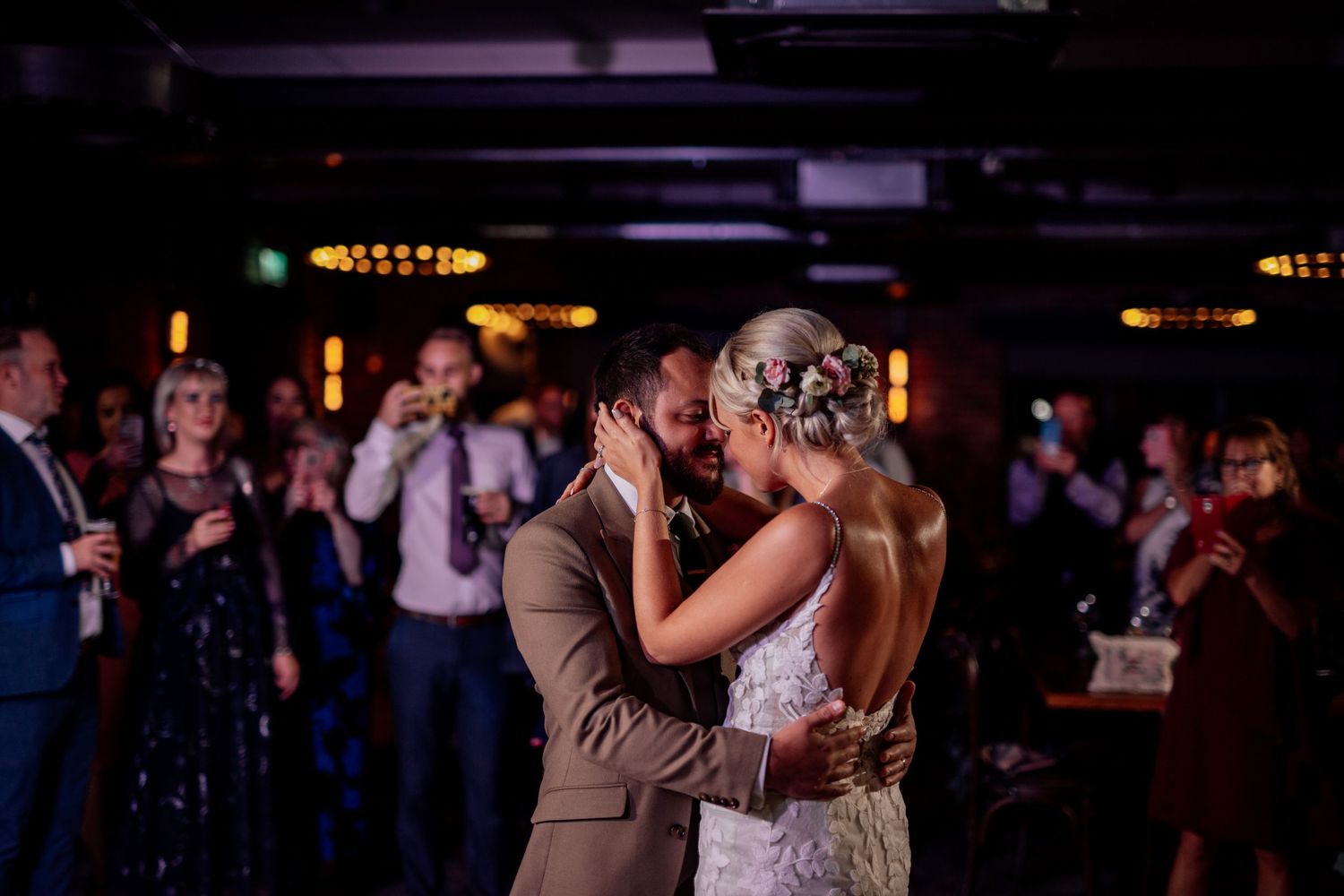 Couples dancing together at a dimly lit wedding reception with purple lighting effects.