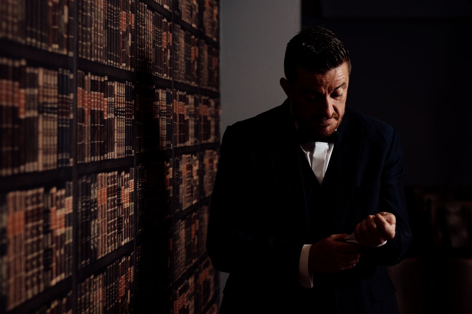 Dramatic silhouette against a wall of books in a dimly lit library setting.