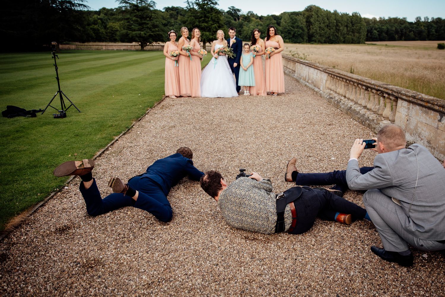 Wedding party lies down playfully on gravel path for creative group photo.