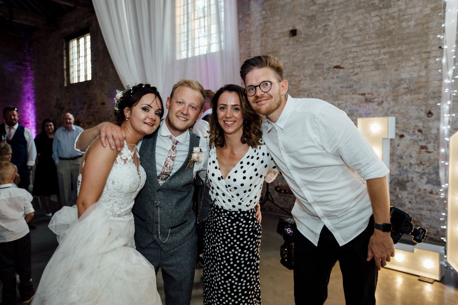 Wedding reception in a rustic brick venue with white draping and dancing guests.