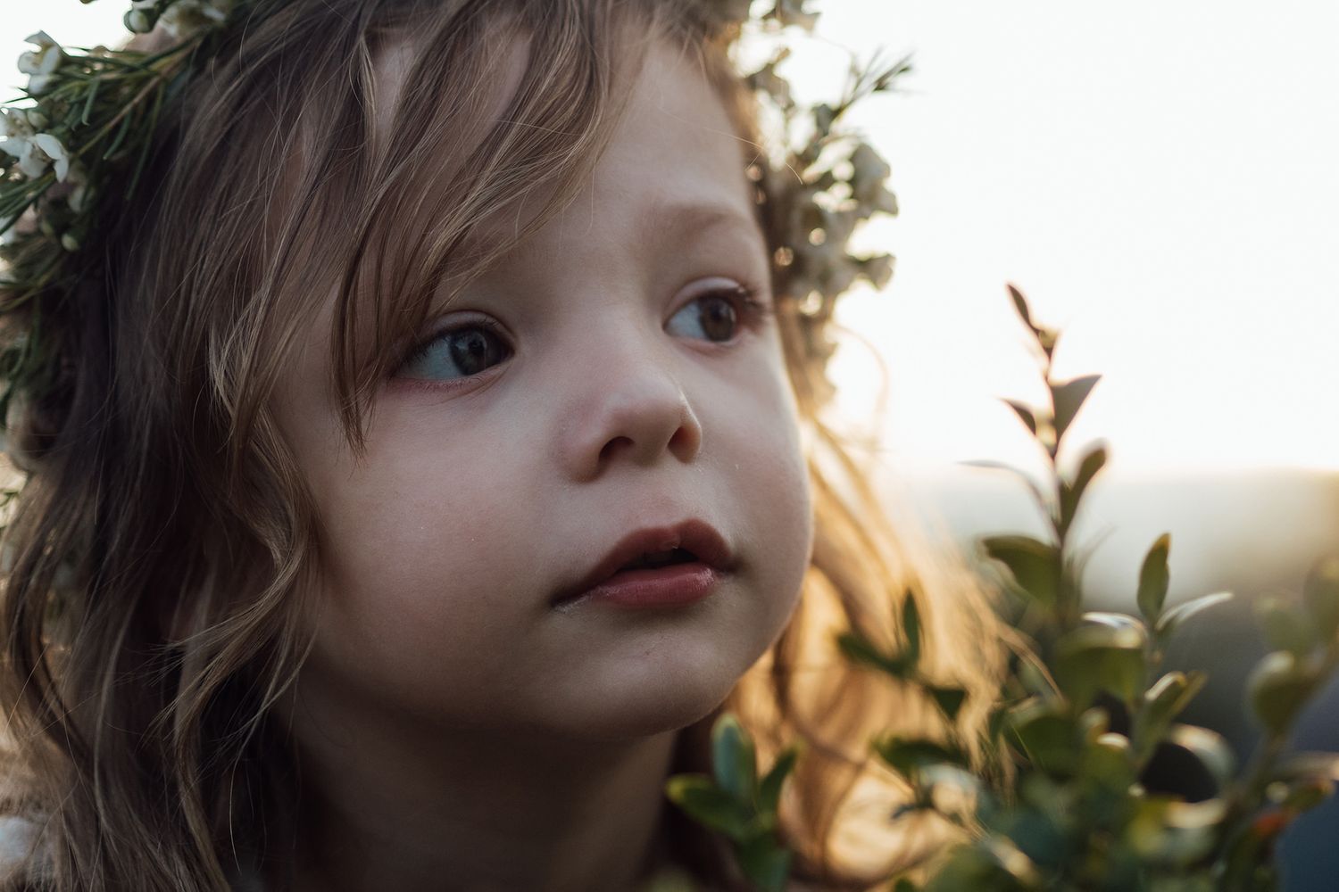 Close-up portrait shot in soft natural lighting with greenery in background.