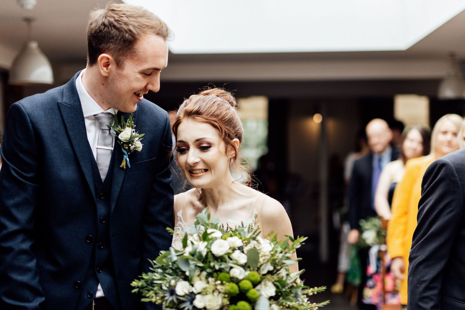 Candid moment between newlyweds with white floral bouquet during wedding ceremony.