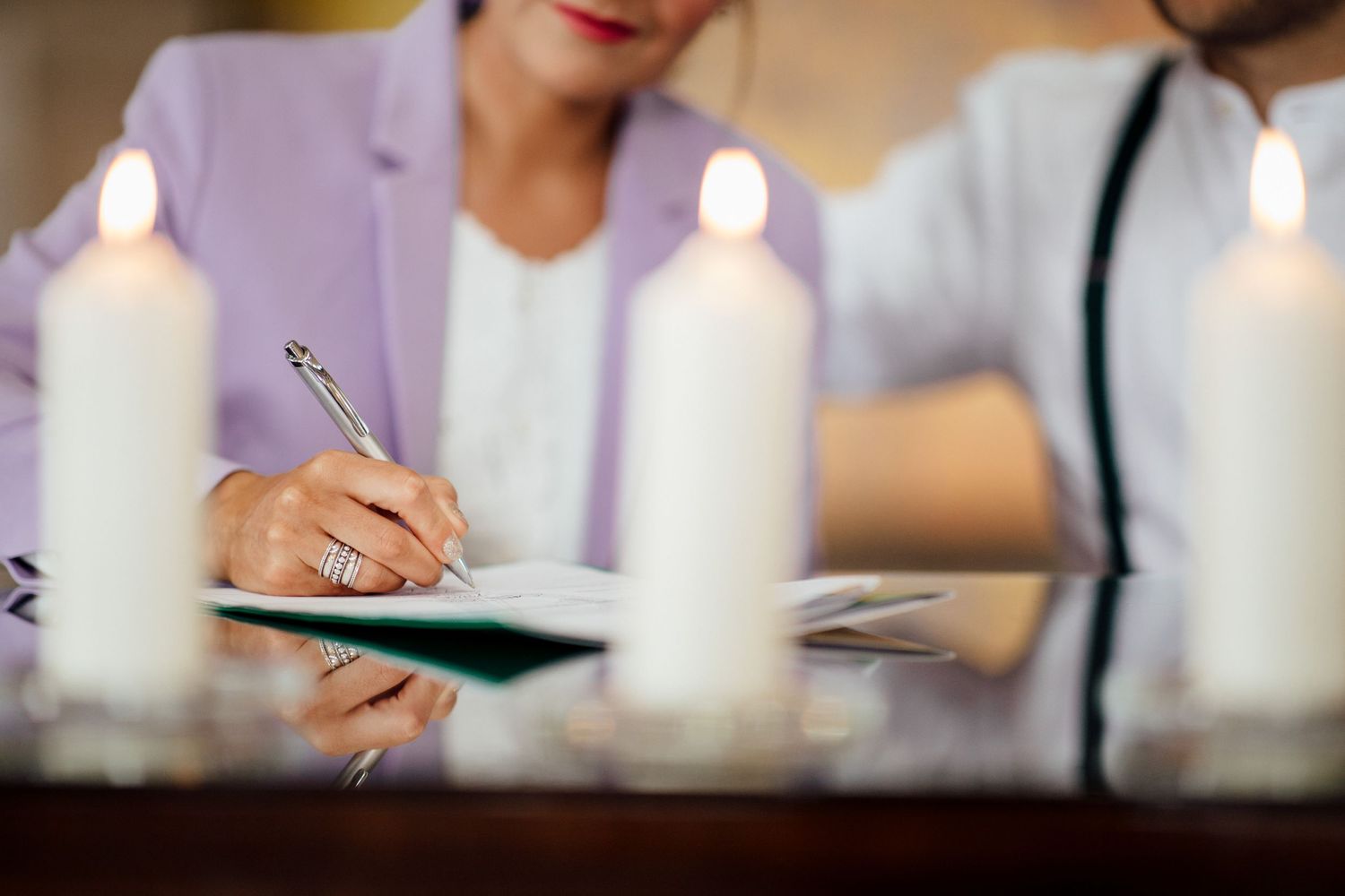 Close-up of hands writing in notebook with lit white candles on table.