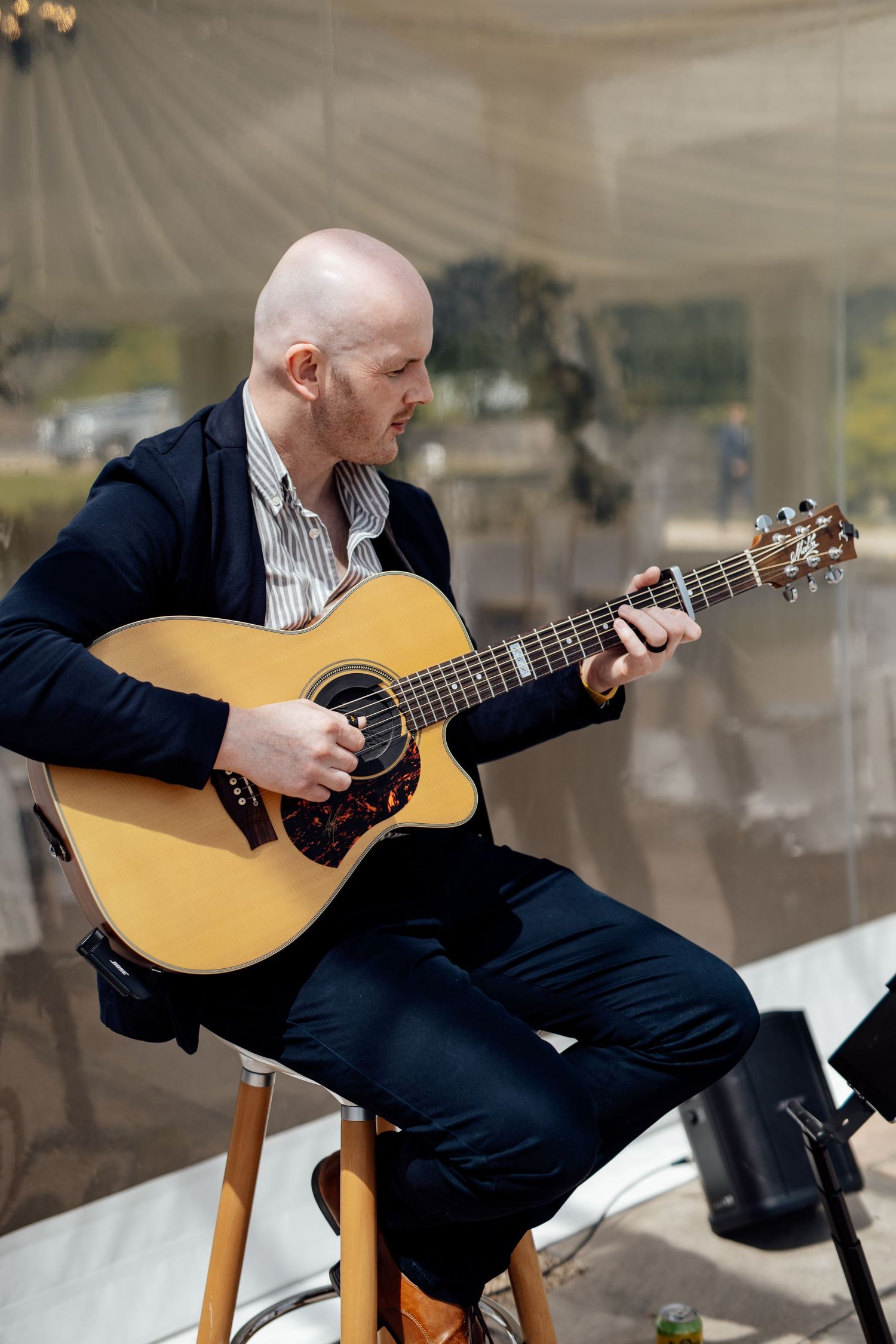 Musician playing acoustic guitar during wedding reception in marquee tent.
