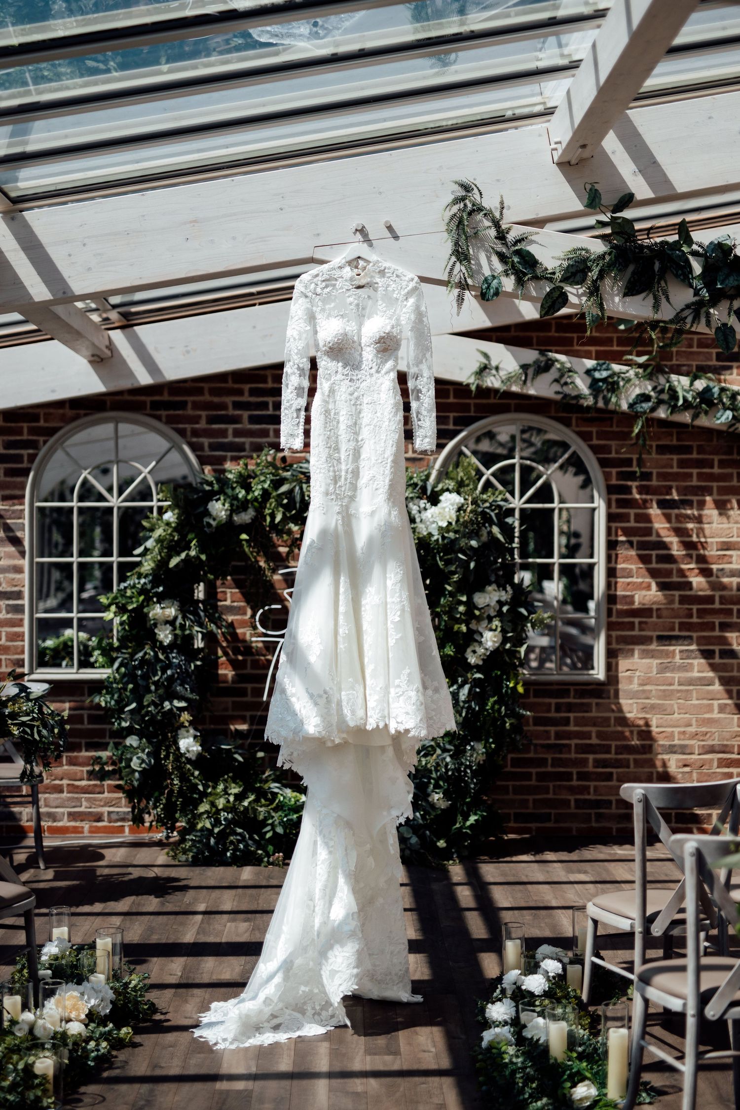 White lace wedding dresses displayed against brick wall with arched windows and greenery.