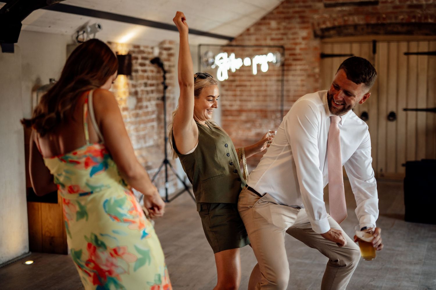 Wedding guests dancing and enjoying themselves at indoor reception with brick walls.