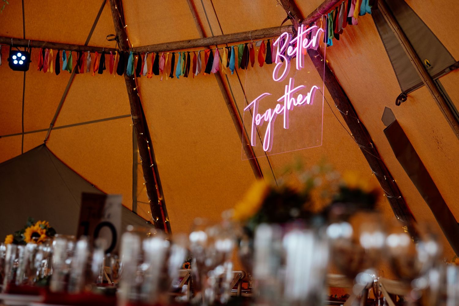 A neon 'Festival' sign glows pink against a tent ceiling with decorative bunting.