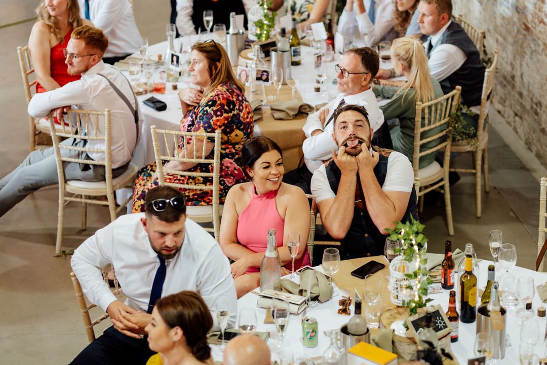 Wedding guests react with emotion and laughter during reception speeches at decorated banquet tables.