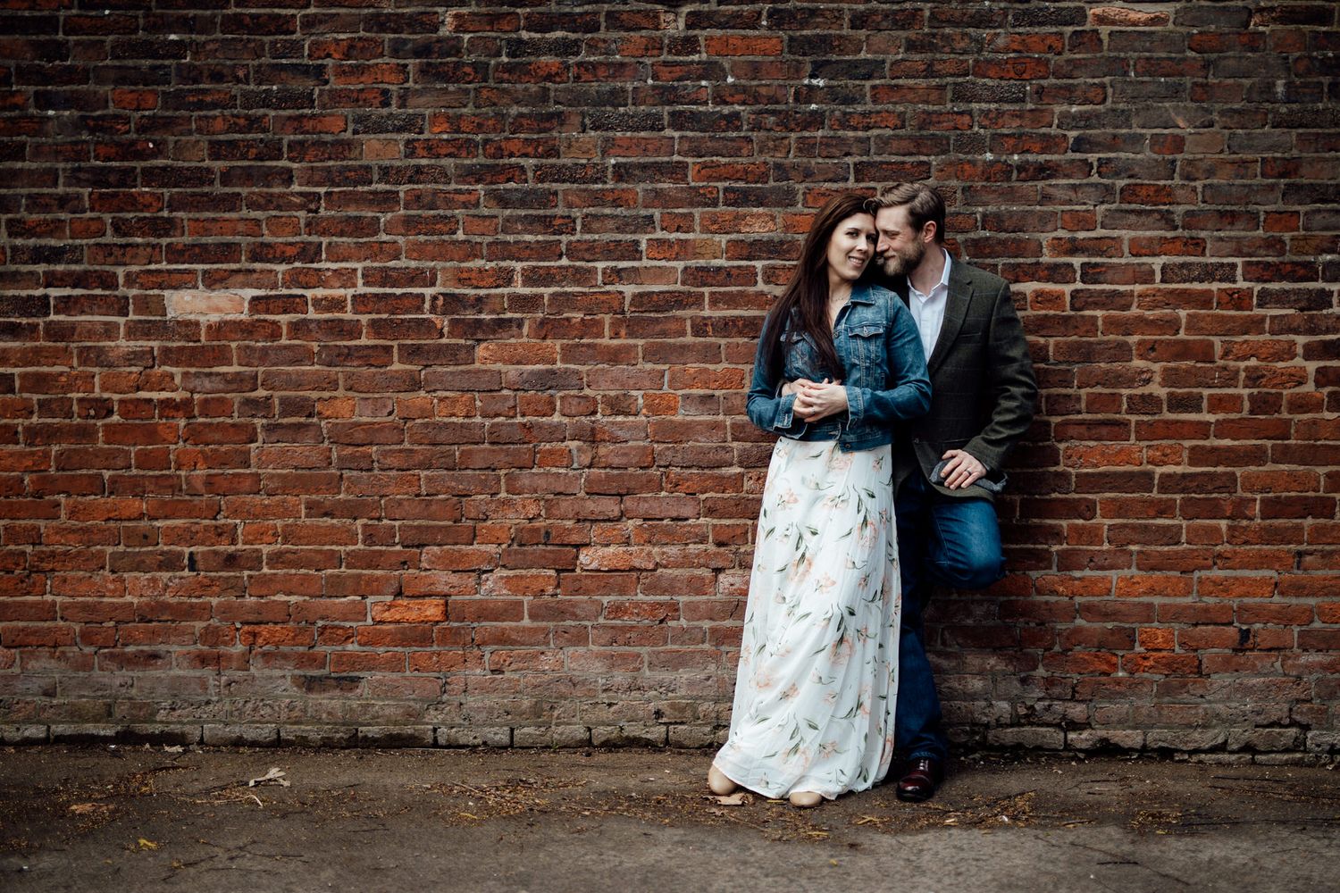 A couple embraces against a weathered red brick wall background.