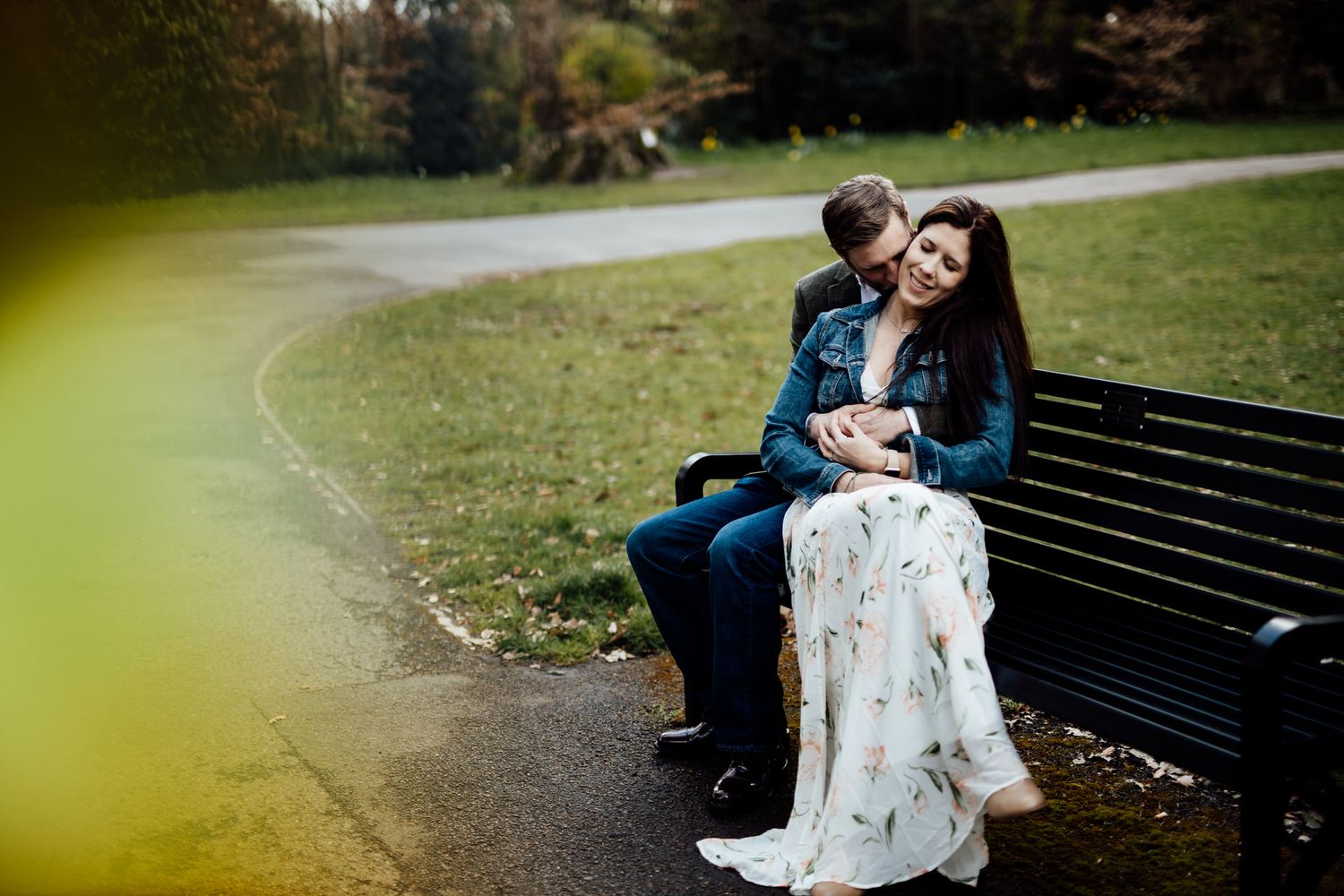 Romantic couple sharing intimate moment on park bench surrounded by greenery.
