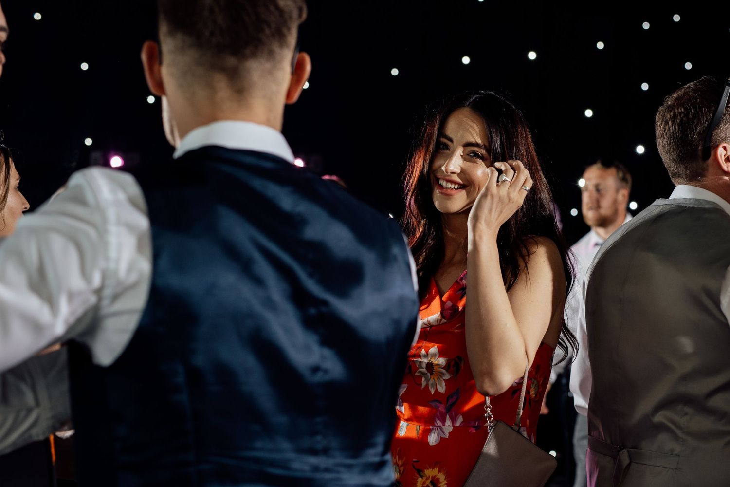 Wedding guests dance and celebrate on a black and white checkered dance floor under twinkling lights.