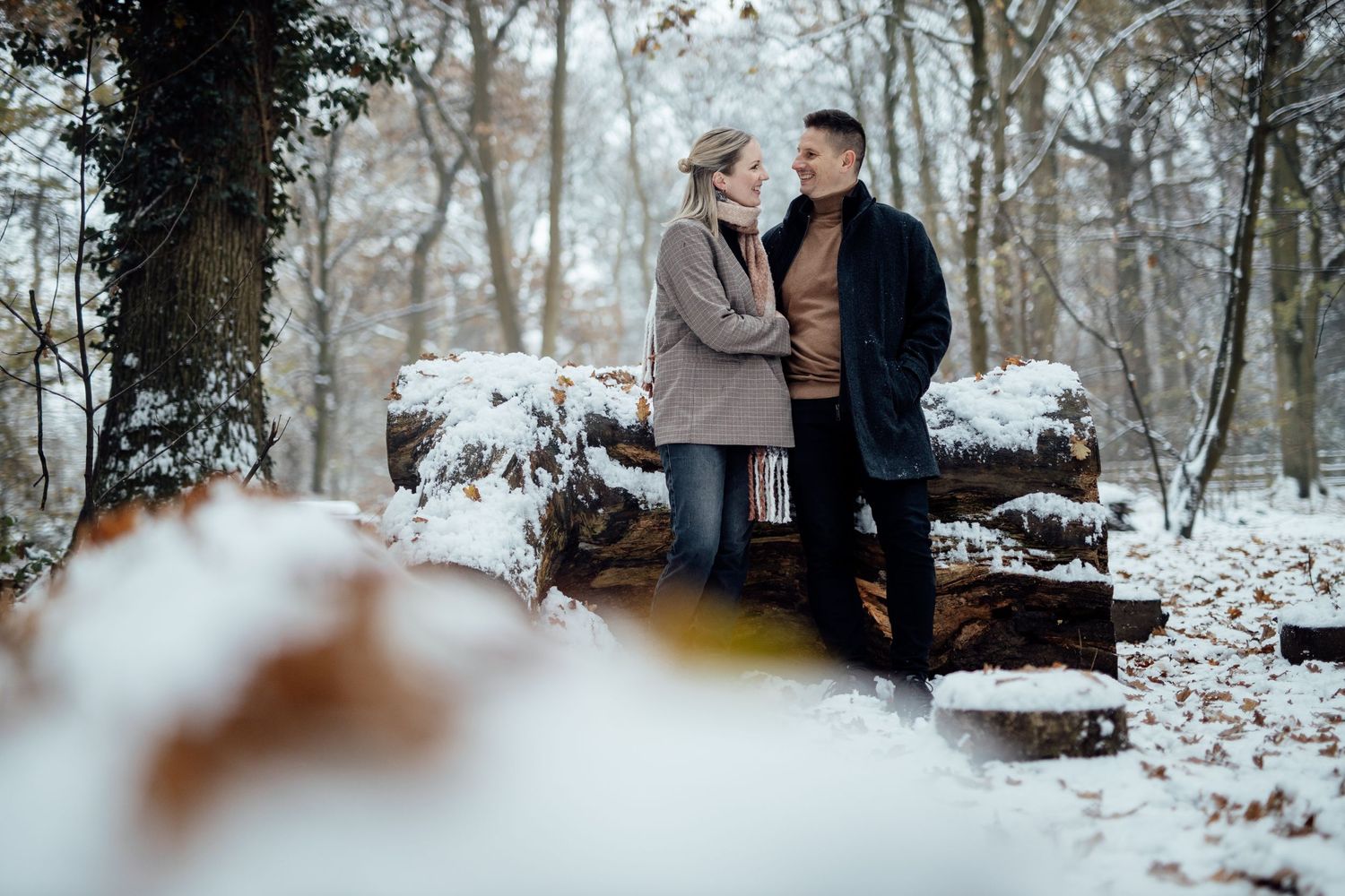 Artistic winter engagement photography with blurred foreground elements in a snowy forest.