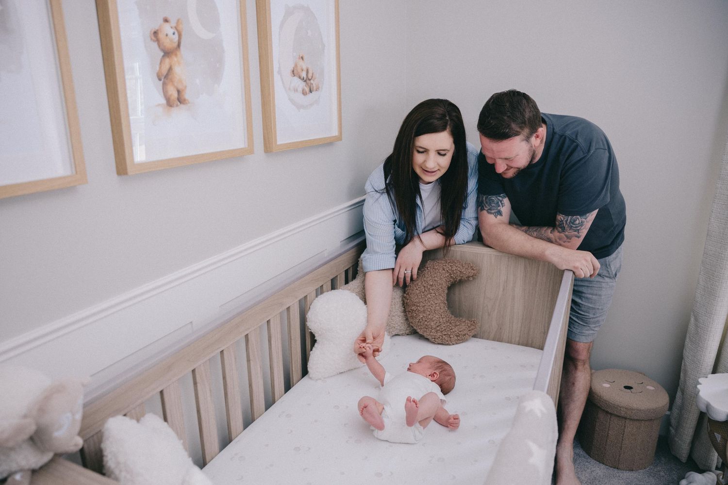 New parents lovingly gaze at their newborn baby lying in a wooden crib in a softly decorated nursery room.