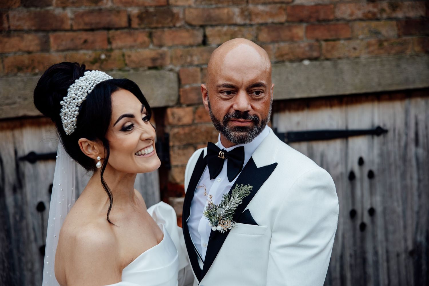 Elegant couple shares intimate moment against industrial brick wall background.