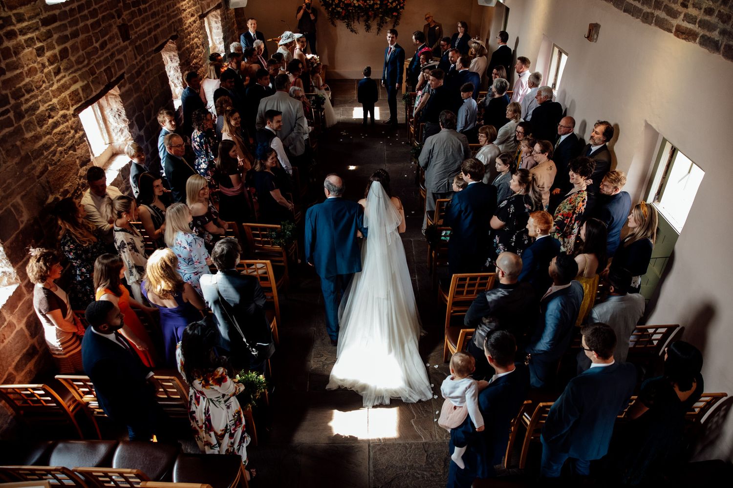 Aerial view of wedding ceremony in rustic brick chapel with guests seated in wooden pews.