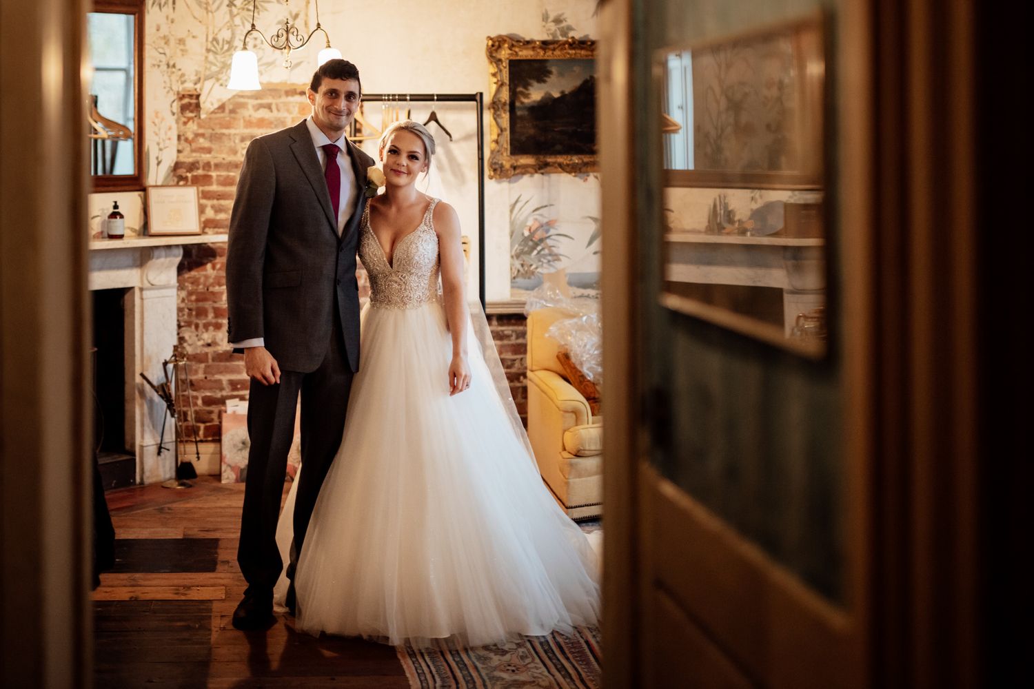 Wedding couple poses in vintage-style hallway with exposed brick walls and natural lighting.