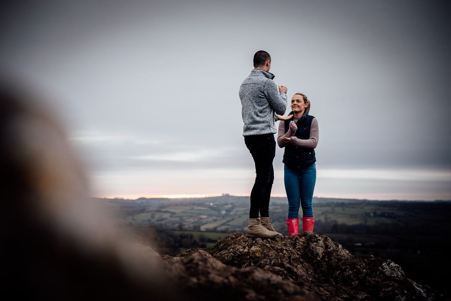 Two people share a romantic moment on a hilltop overlooking a misty landscape.