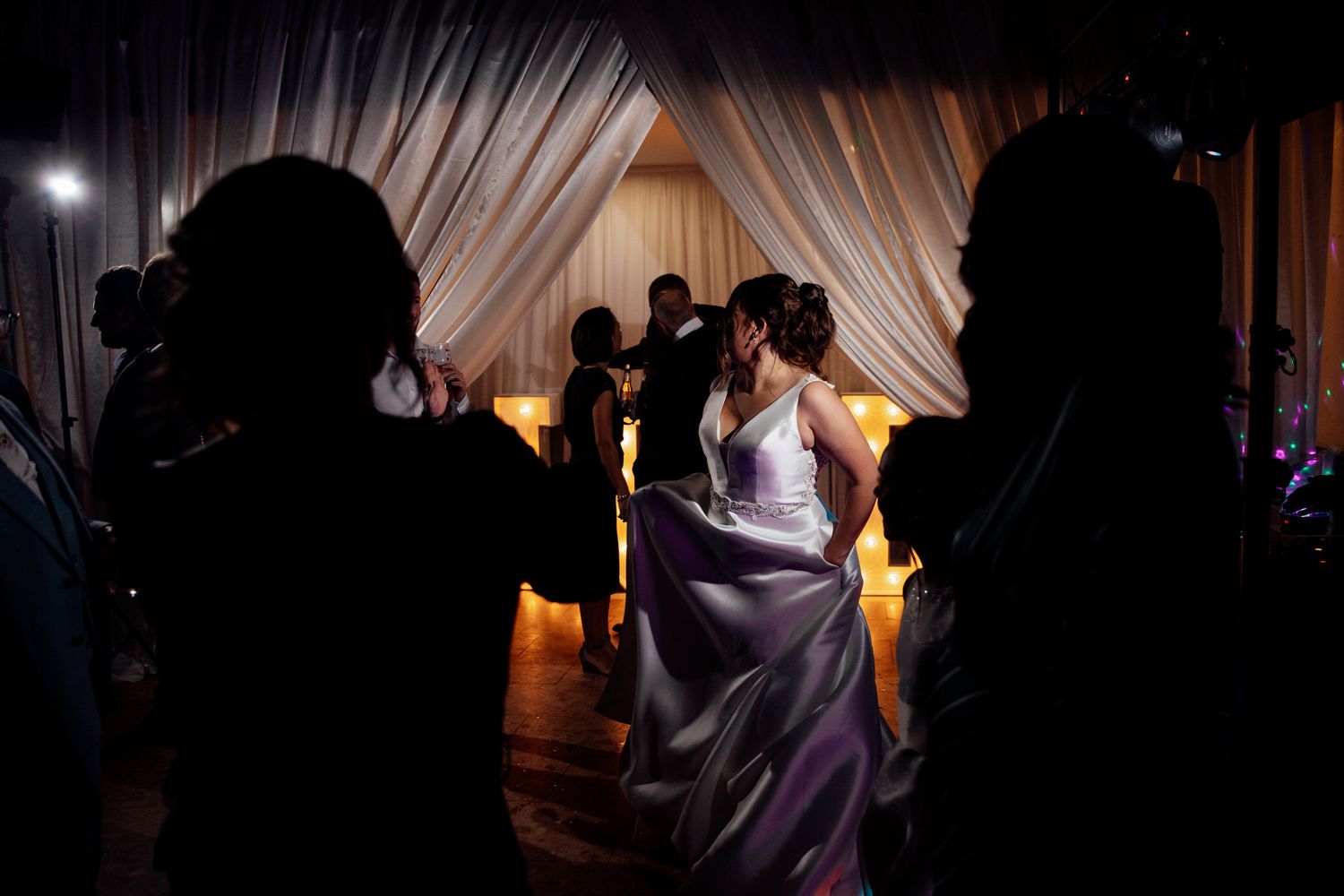 Silhouettes of wedding guests dancing against backlit white drapes at an evening reception.