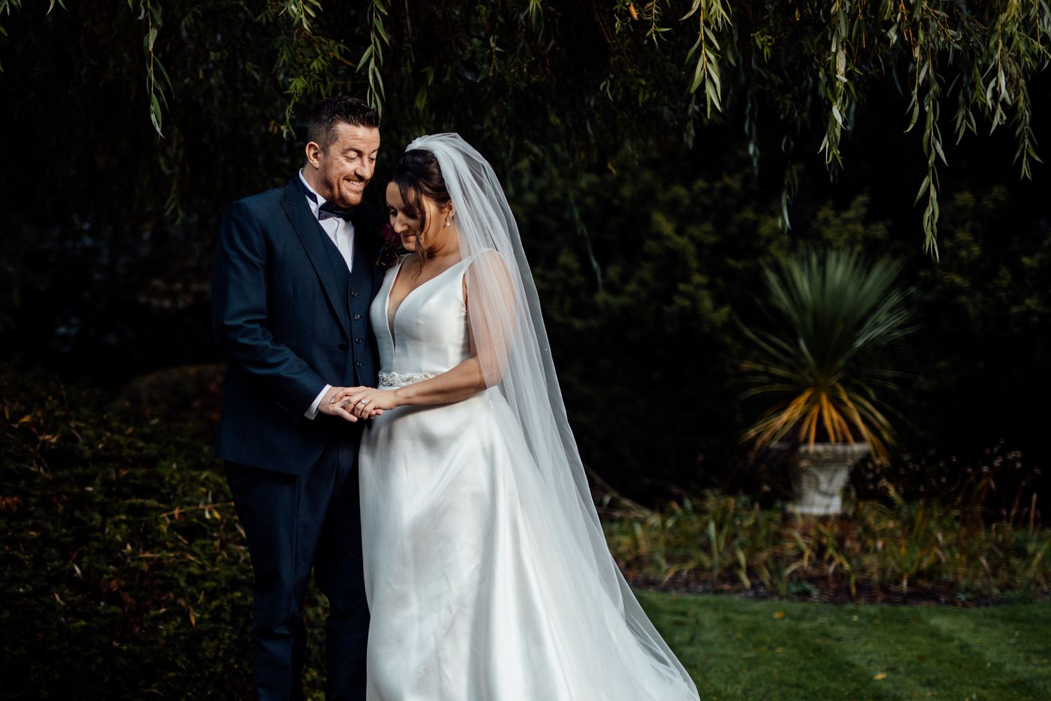 Romantic wedding portraits under weeping willow trees in a garden setting.