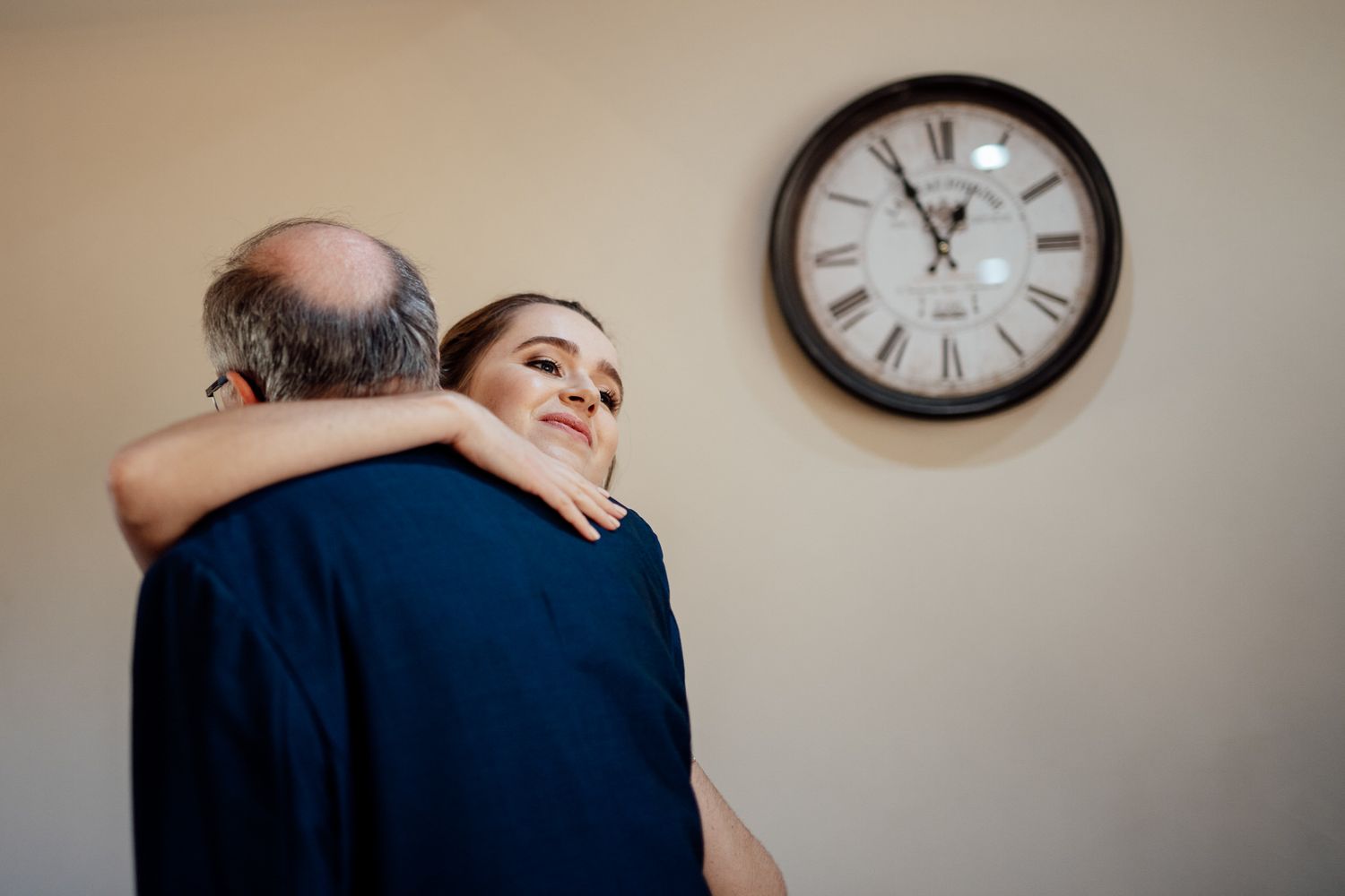 Wedding party sharing candid laughs beside vintage wall clock.