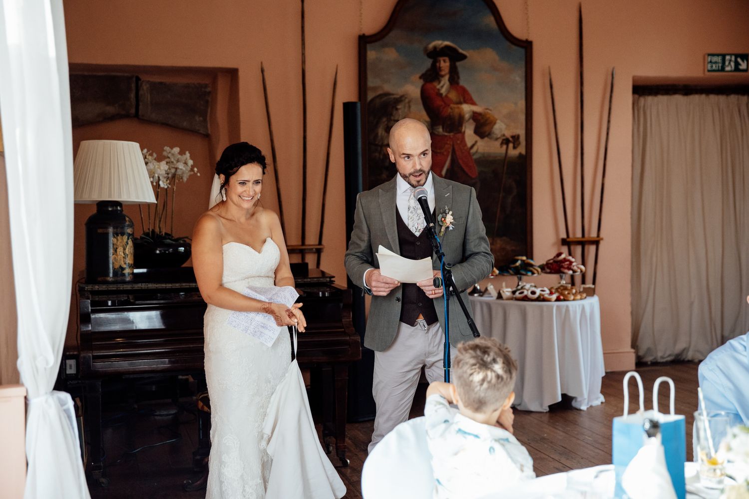 Wedding party poses in front of rustic brick wall venue with string lights and elegant decor.