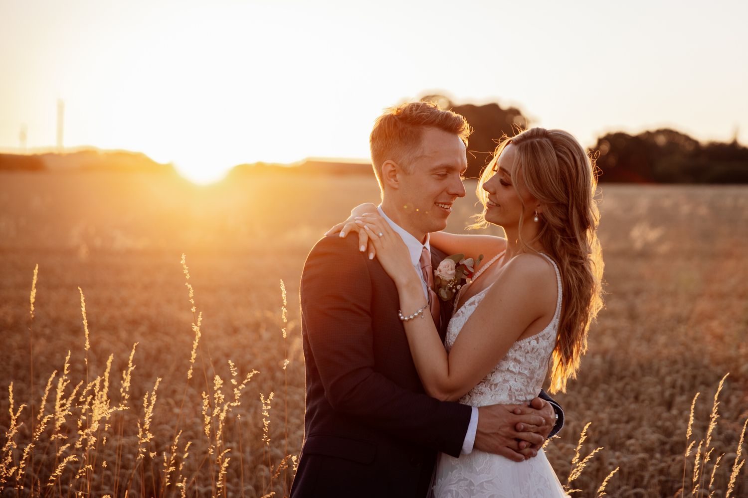 A romantic wedding couple embraces in a golden wheat field at sunset creating a dreamy silhouette.
