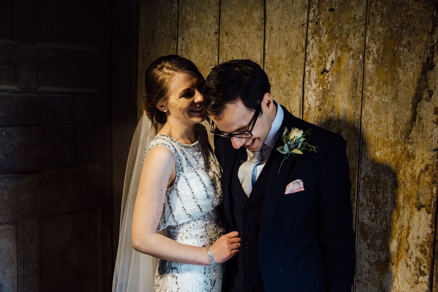 Intimate wedding portraits against weathered wooden walls with dramatic lighting.