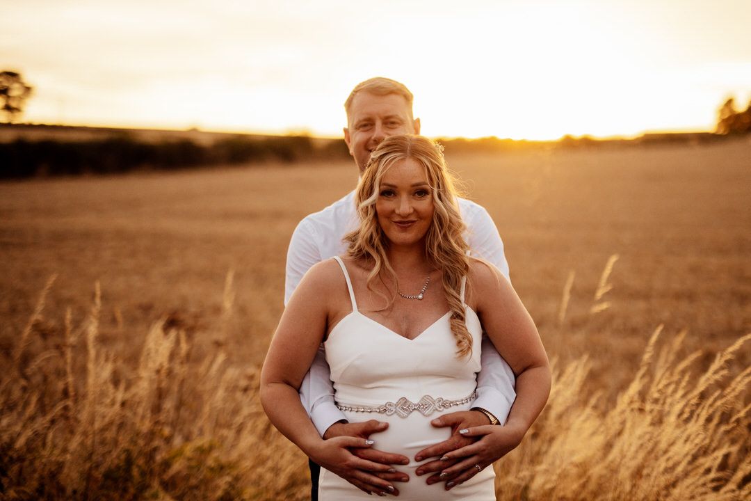 Bride poses in a white dress during golden hour sunset in a wheat field.