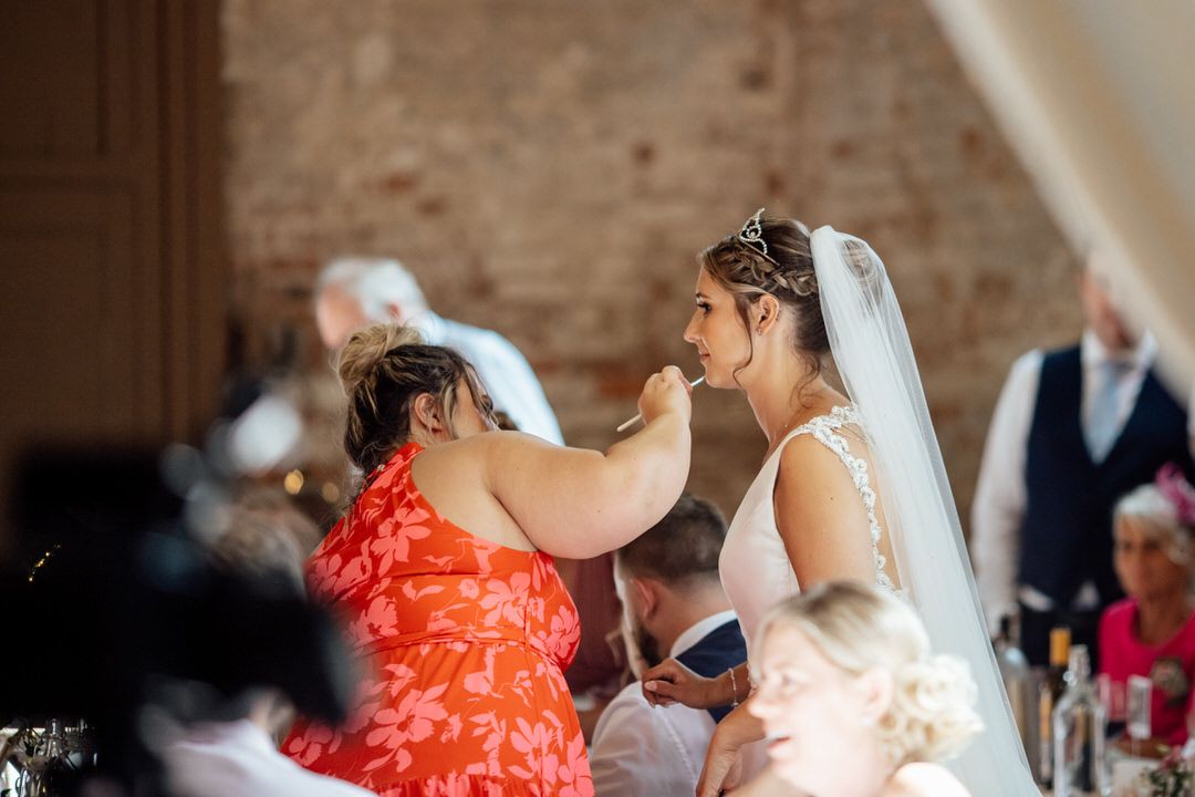 Wedding guests laugh and react emotionally during speeches at an indoor reception with exposed brick walls.