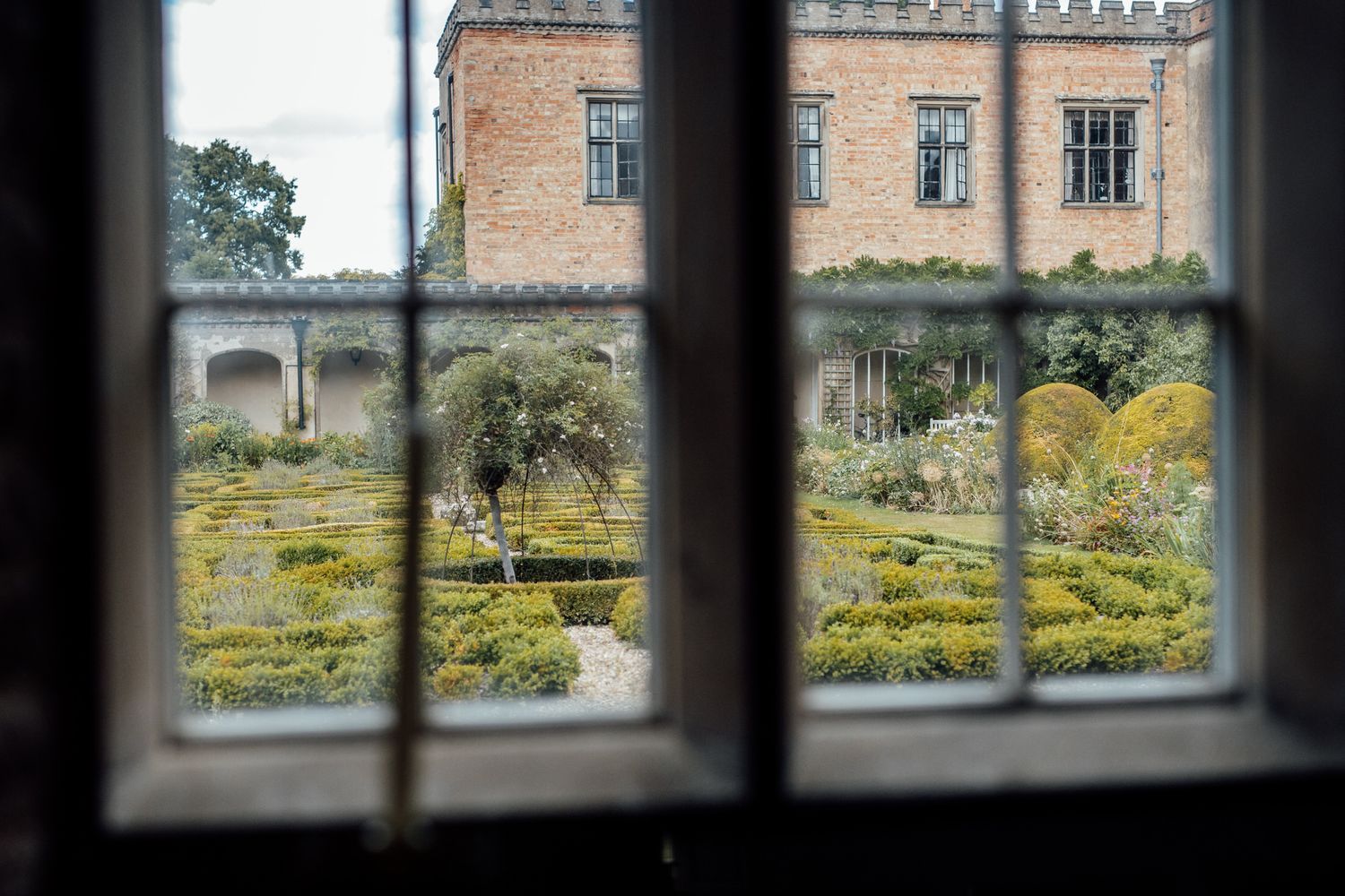 View through a window pane of a historic mansion's manicured garden and architecture.