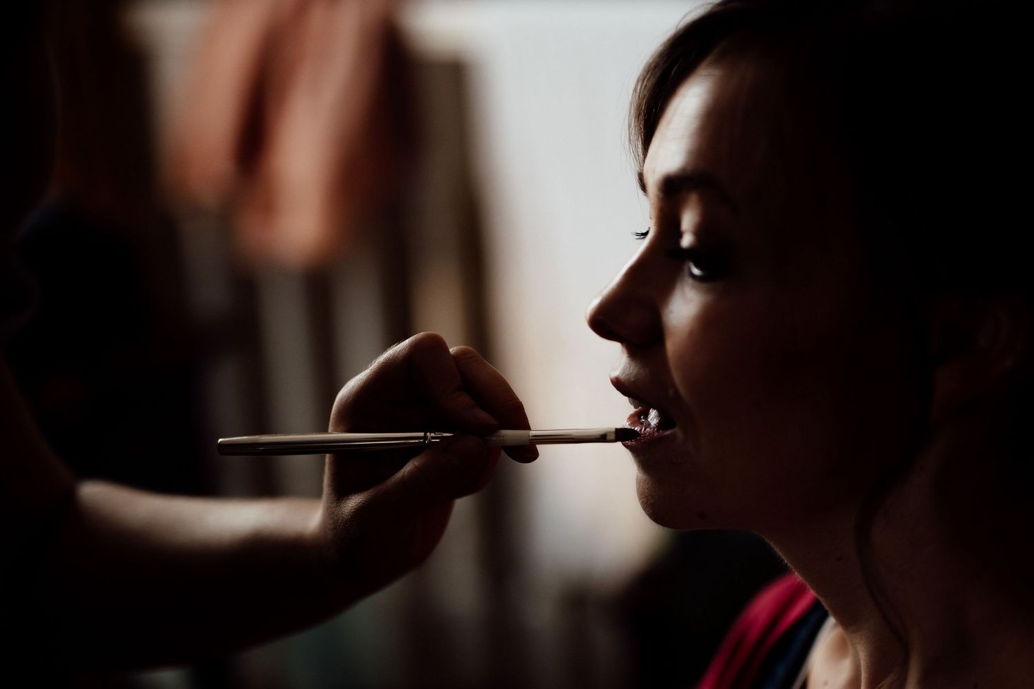 Silhouette of someone having makeup applied with a brush in dramatic lighting.
