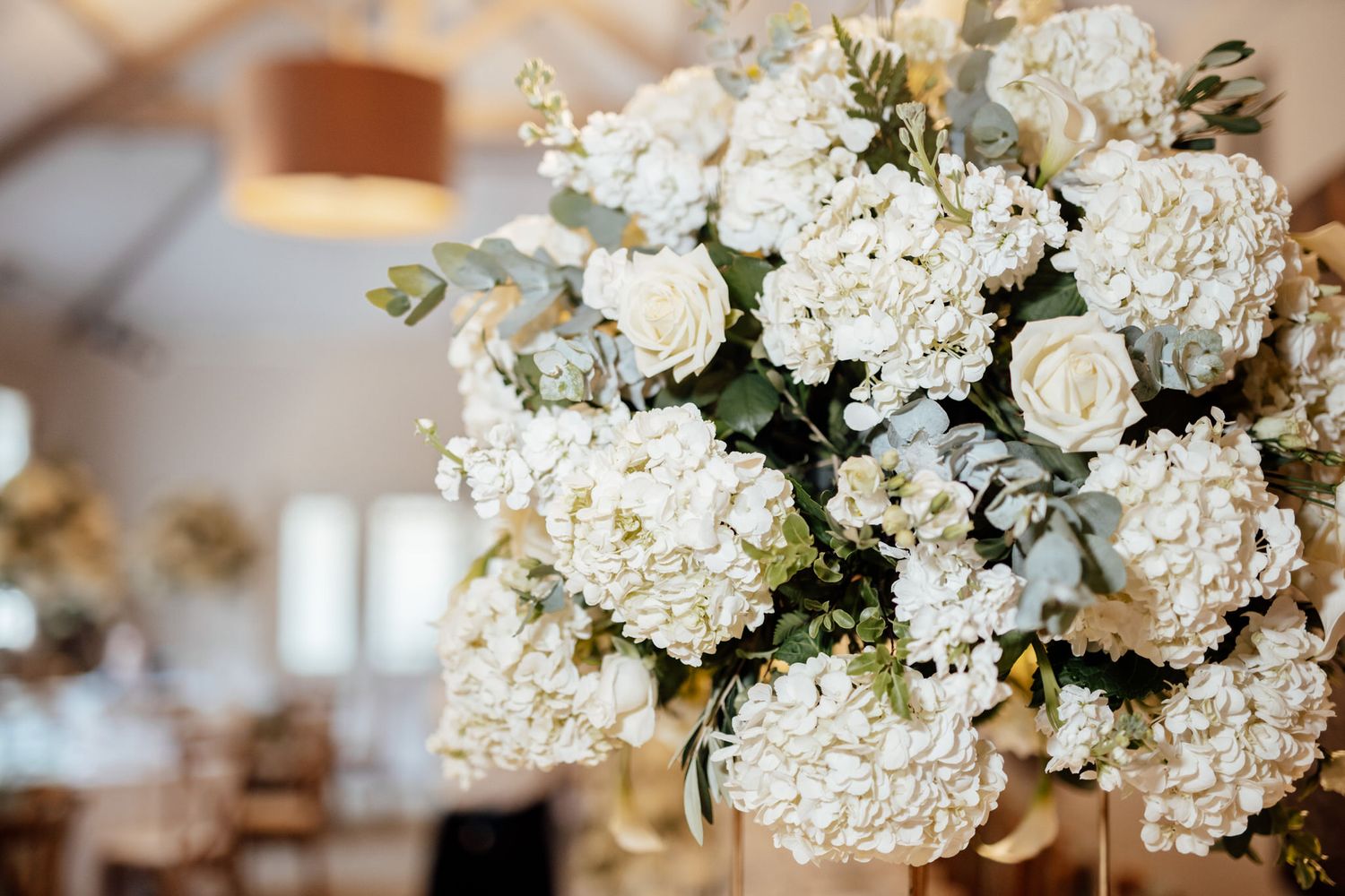 White hydrangea and rose floral centerpieces arranged on tables at wedding reception.